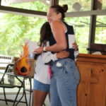 Two women hugging warmly indoors near a wooden table.